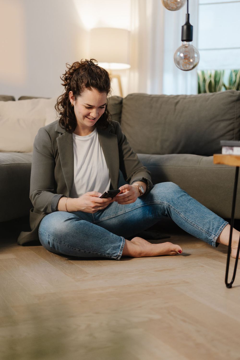 Sandra sitzt am Sofa und schaut lachend aufs Handy