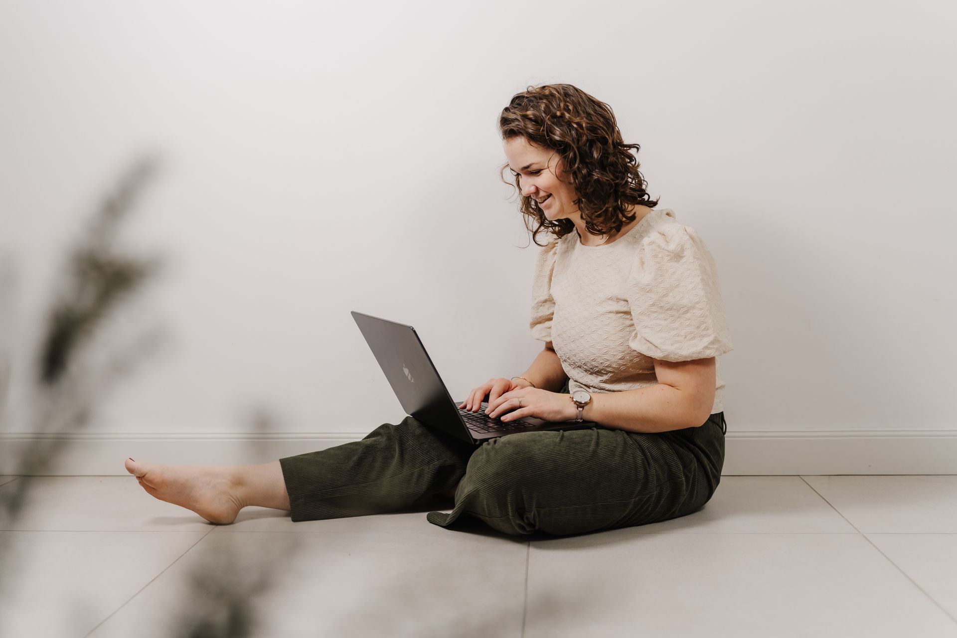 Sandra sitzt barfuß mit Laptop auf dem Boden und lacht